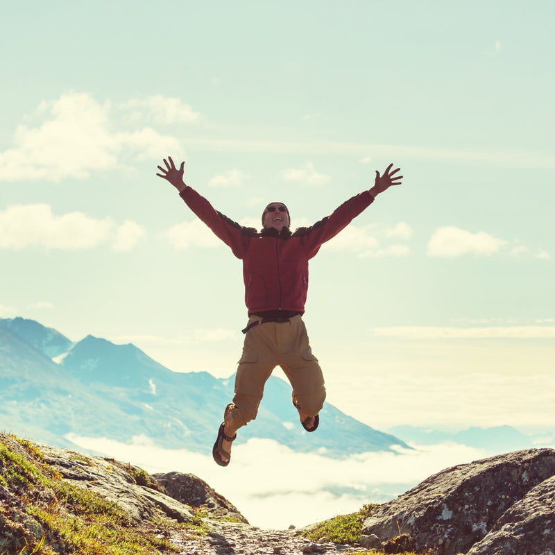 Person jumping with arms outstretched against a mountainous landscape